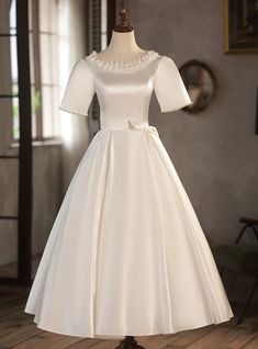 a white dress on a mannequin stand in front of a wall and window