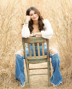 a woman sitting on top of a wooden chair in the middle of a grass field