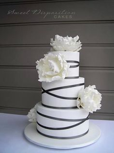 a three tiered cake with white flowers on top and black stripes around the edges