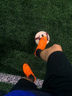 a person wearing orange and black shoes standing next to a soccer ball