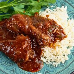 a blue plate topped with rice and meat covered in gravy on top of greens