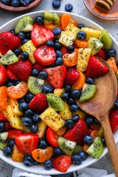 a white bowl filled with sliced fruit next to a wooden spoon