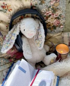 a stuffed rabbit sitting on top of a bed next to an open book and candle