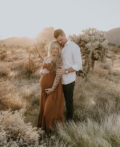 a man and woman standing next to each other in a field with cacti