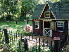 a small red and white house sitting in the middle of a lush green field next to a black fence