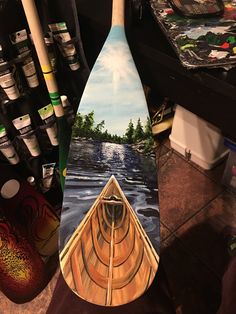 a painting of a canoe on the side of a surfboard with water and trees painted on it