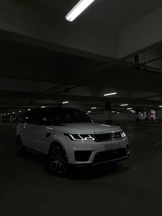 a white range rover is parked in a parking garage at night time with its lights on