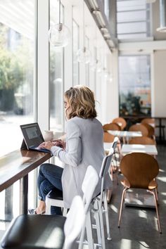 a woman sitting at a table with a laptop in her lap looking out the window