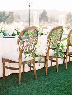 the chairs are lined up on the grass for an outdoor dinner table with white linens and greenery