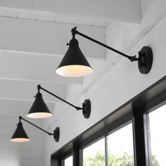 three black and white lights hanging from the ceiling in a room with two large windows