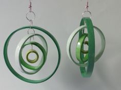 two green and white circular earrings hanging from hooks on a hook chain with rings attached to them