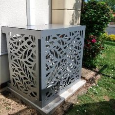 a metal box sitting on the side of a building next to a flower bed and shrubbery