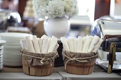 two baskets filled with white napkins sitting on top of a table next to plates and cups