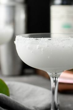 a close up of a margarita in a coupe glass with salt and lime on the rim