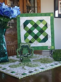 a green vase with blue flowers sitting on top of a table next to a quilt