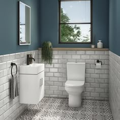 a white toilet sitting next to a sink in a bathroom under a window with blue walls