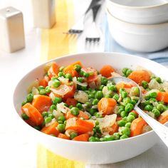 a bowl filled with peas and carrots next to a fork on top of a table