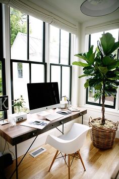 a computer desk sitting in front of a window next to a potted plant on top of a wooden table