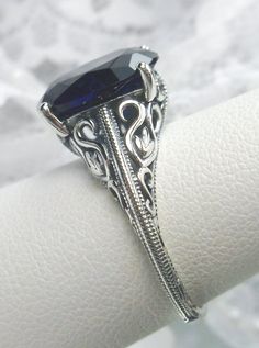 Blue Sapphire Sterling Silver Ring Swan Design #D190 Introducing our Blue Sapphire Sterling Silver Ring, Swan Design #D190 - a mesmerizing fusion of Art Deco elegance and contemporary flair. Crafted with precision and passion, this stunning ring boasts a radiant man-made blue sapphire gemstone, set within a sterling silver filigree setting that exudes sophistication and charm. At the heart of this exquisite piece lies a faceted simulated oval gemstone, measuring 12mm x 10mm, captivating with its Elegant Blue Sapphire Ring For Formal Occasions, Elegant Sapphire Jewelry With Intricate Design, Elegant Blue Sapphire Ring, Elegant Artistic Design Jewelry For Anniversary, Elegant Artistic Jewelry For Anniversary, Unique Blue Sapphire Ring For Wedding, Adjustable Elegant Sterling Silver Sapphire Ring, Elegant Blue Jewelry With Intricate Design, Formal Sapphire Filigree Ring With Intricate Design