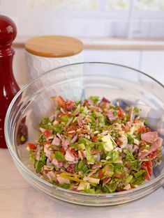 a glass bowl filled with chopped vegetables on top of a counter next to a red pepper shaker