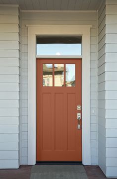 an orange front door with two sidelights on a white house in the day light