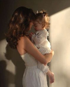 a woman holding a baby in her arms and wearing a white dress with ruffles