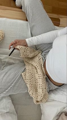 a woman laying on top of a bed next to a white blanket and a ball of yarn