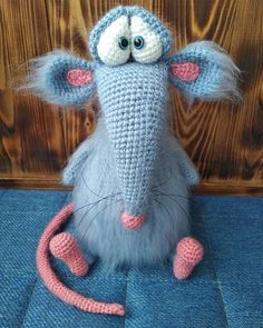 a crocheted rat sitting on top of a blue cloth covered floor next to a wooden wall