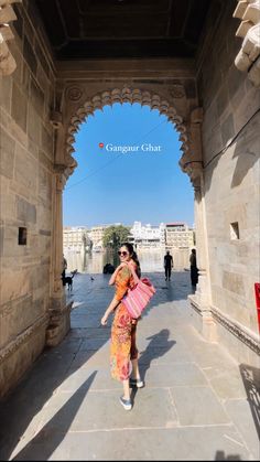 a woman in an orange and pink sari walking down a walkway with her handbag