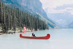 a man and woman in a canoe on a lake surrounded by mountains with pine trees