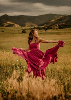 a woman in a red dress is standing in a field with her arms spread out