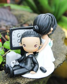 a bride and groom figurine sitting next to a small clock on a rock