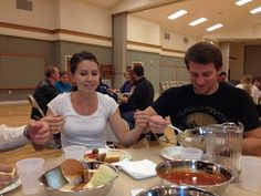 three people sitting at a table with plates of food in front of them and one person holding their hands out