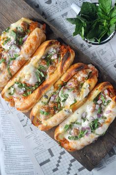 several breads with cheese and toppings are on a cutting board next to a bowl of herbs