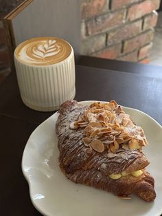 a piece of cake on a plate next to a cup of cappuccino