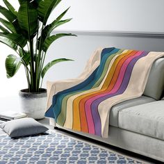 a couch with a rainbow blanket on it next to a potted plant and rug