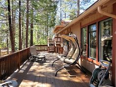 two lawn chairs sitting on a wooden deck next to a building with trees in the background