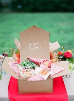 a table topped with a box filled with food next to a lush green park covered in trees