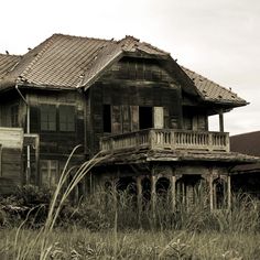 an old abandoned house in the middle of a field with grass and weeds growing around it