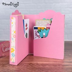 an open pink folder with some cards in it on top of a wooden table next to a sign that says simply crafty