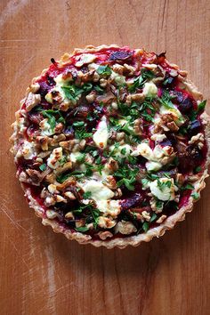 a pie with nuts, cheese and greens on it sitting on a wooden table top