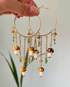 These earrings feature gold hoops adorned with dangling mushrooms, accented by orange beads and small green leaves for a whimsical and fairy-inspired look Size: 13.5*5.5 cm/ 5.3*2.2 in Fairycore Mushroom, Indie Accessories, Mushroom Earring, Inspiring Drawings, Mushroom Beads, Accessories Y2k, 90's Aesthetic, Fairy Earrings, Aesthetic Accessories