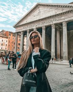 a woman is standing in front of an old building with columns and people walking around