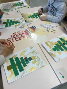 several children are sitting at a table working on art projects with yellow and green paint