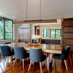 a dining room table surrounded by blue chairs and wooden flooring with large windows in the background