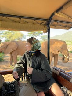 a woman sitting in the back of a vehicle with an elephant behind her