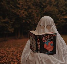 a person in a white ghost costume reading a book with glasses on their head and covering his face