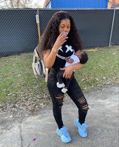 a woman holding a baby in her arms while standing next to a chain link fence