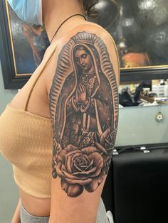 a woman with a tattoo on her arm holding a rose and an image of the virgin mary