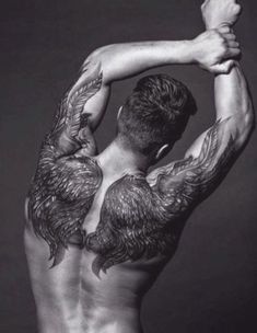 the back of a man with tattoos on his arms and chest, holding up something